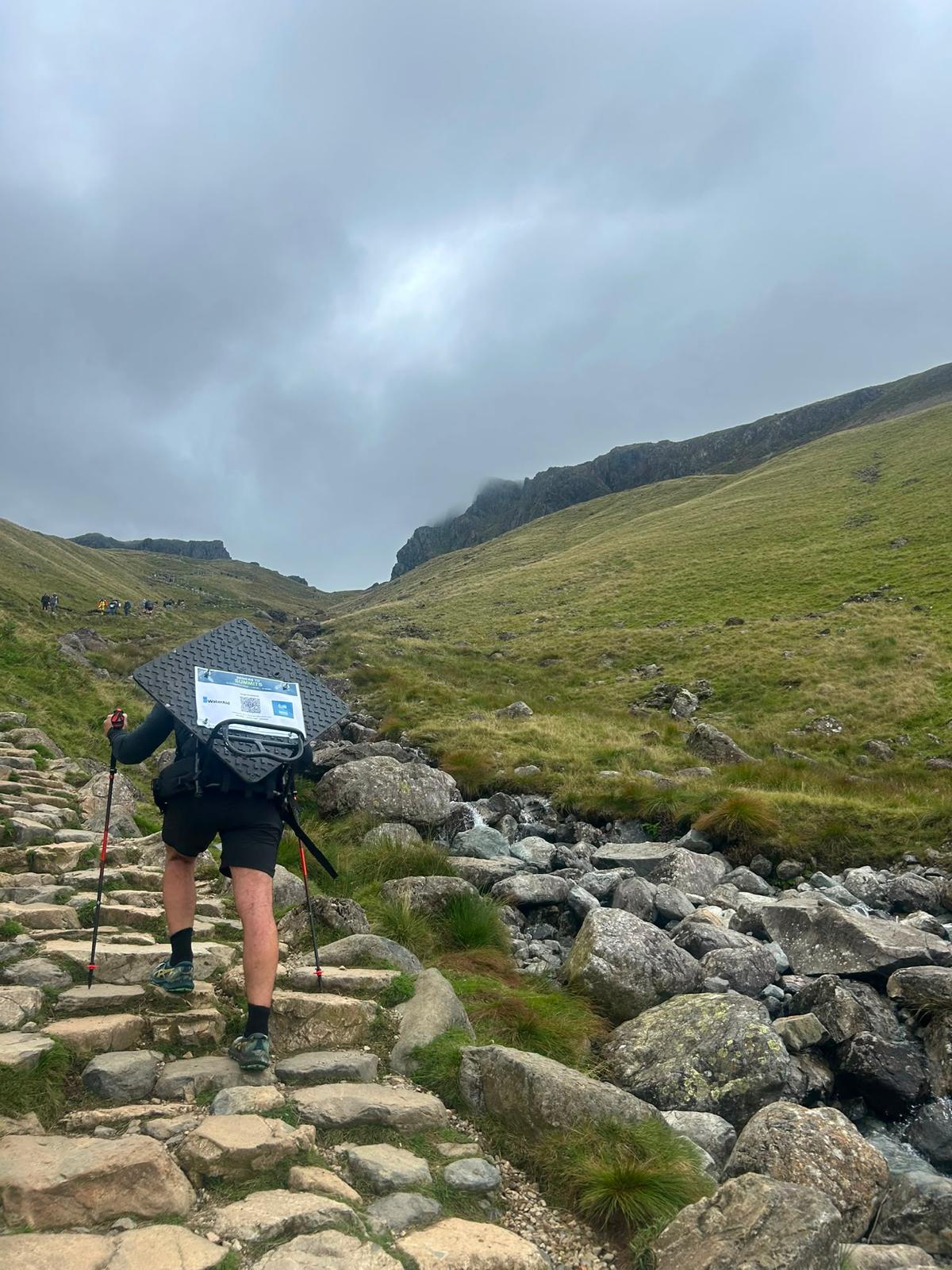 Sewers to Summits participant carrying a 24 kg manhole cover up a rocky mountain route