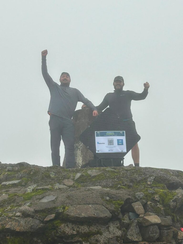Two Sewers to Summits charity challenge participants celebrating beside the manhole cover on a misty mountain summit