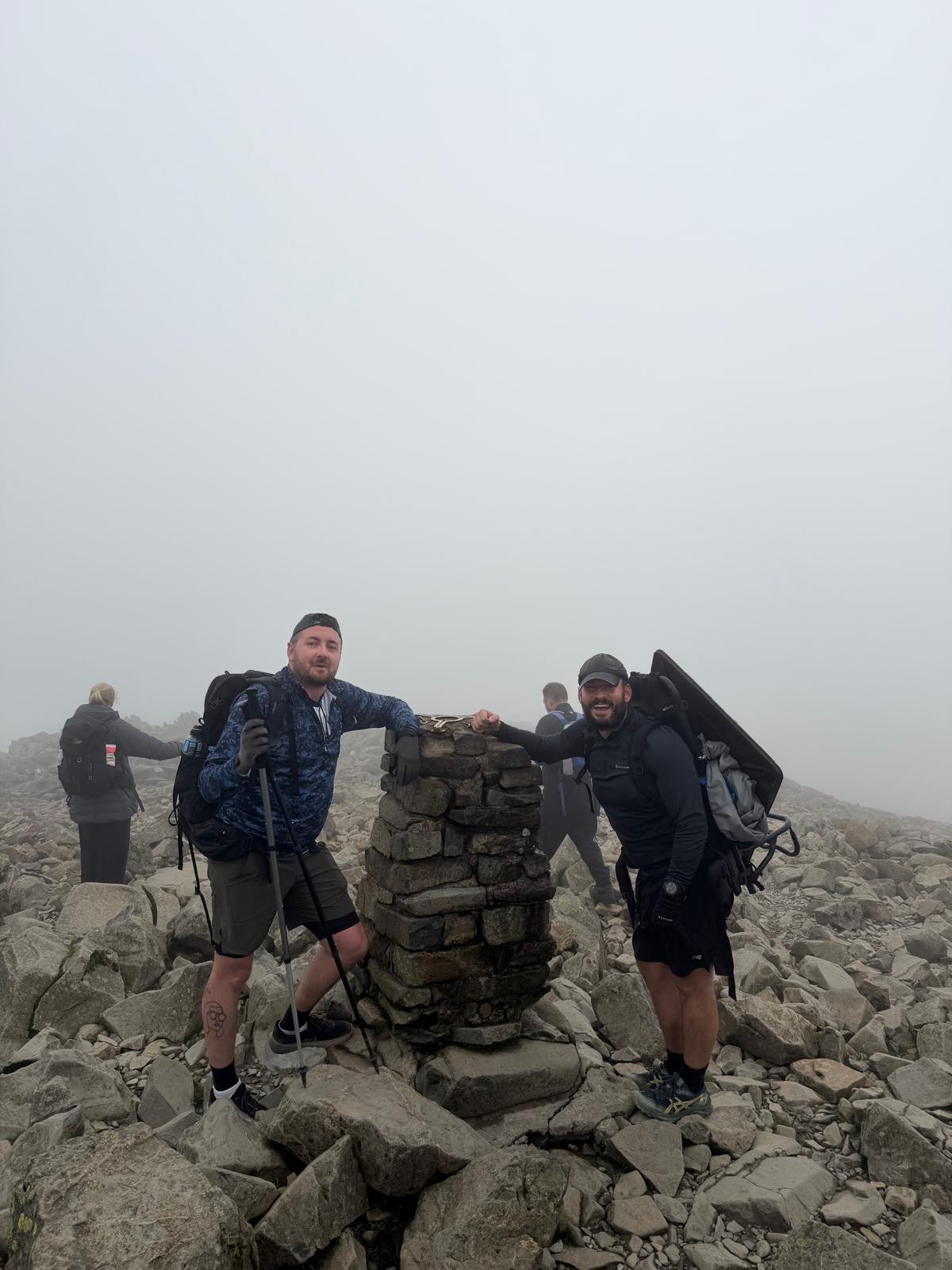 Two Sewers to Summits walkers at a rocky mountain summit cairn