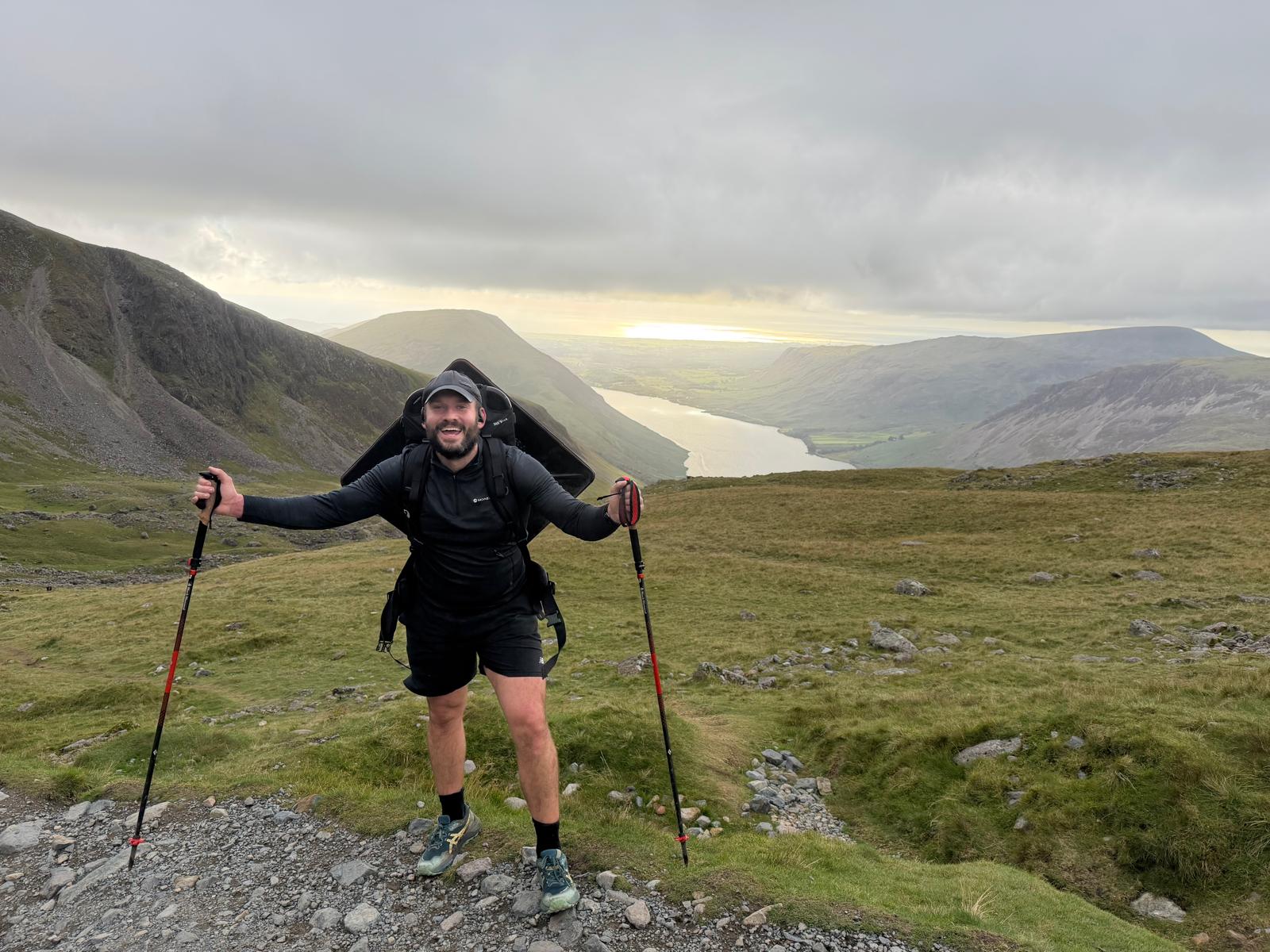Walker with trekking poles carrying the charity manhole cover above a mountain valley